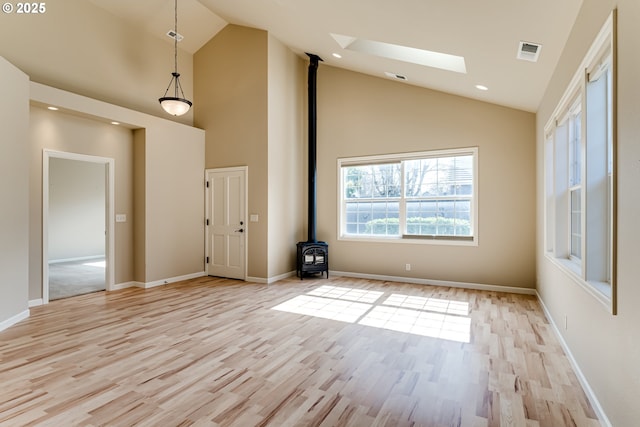 interior space featuring visible vents, light wood finished floors, high vaulted ceiling, a wood stove, and a skylight