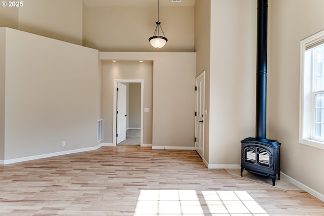 unfurnished living room featuring a wood stove, light wood-style flooring, a high ceiling, and a wealth of natural light