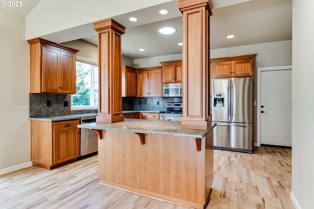 kitchen with stainless steel appliances, light wood-style floors, a breakfast bar, and ornate columns