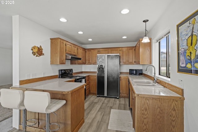 kitchen with black appliances, under cabinet range hood, a sink, a peninsula, and light wood finished floors