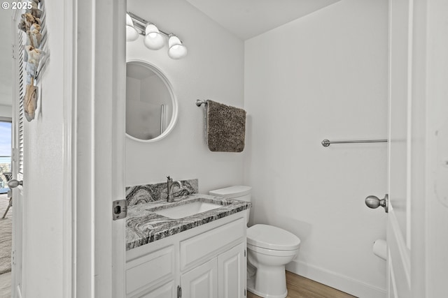 bathroom featuring toilet, vanity, baseboards, and wood finished floors