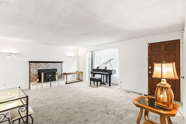 carpeted living room featuring a stone fireplace and a textured ceiling