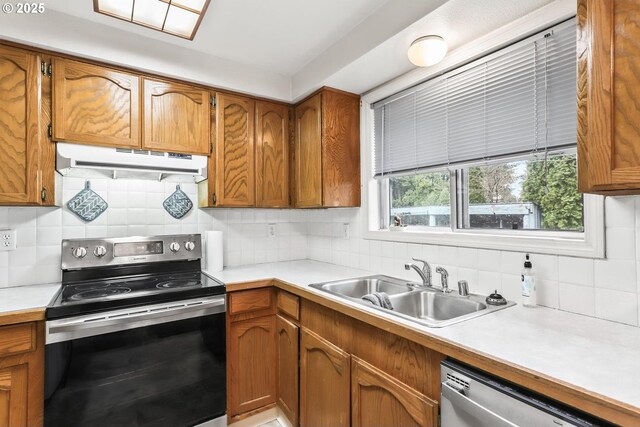 kitchen featuring under cabinet range hood, light countertops, brown cabinets, appliances with stainless steel finishes, and a sink