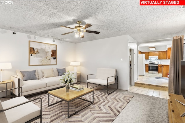 living area with a textured ceiling, light tile patterned floors, a ceiling fan, and light carpet