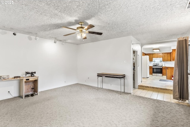 unfurnished living room featuring light tile patterned floors, a ceiling fan, baseboards, a textured ceiling, and light carpet