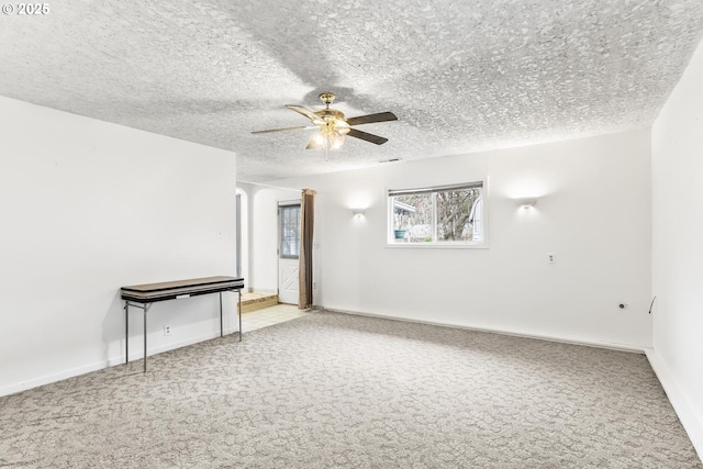 carpeted empty room with baseboards, a textured ceiling, and a ceiling fan