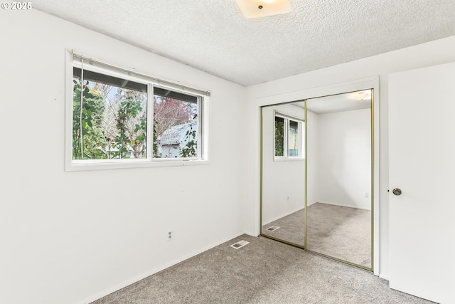 unfurnished bedroom featuring visible vents, a closet, carpet floors, and a textured ceiling