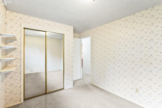 unfurnished bedroom featuring a closet, wallpapered walls, a textured ceiling, and carpet