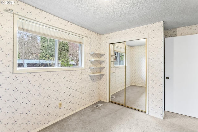 unfurnished bedroom featuring multiple windows, a textured ceiling, carpet flooring, and wallpapered walls