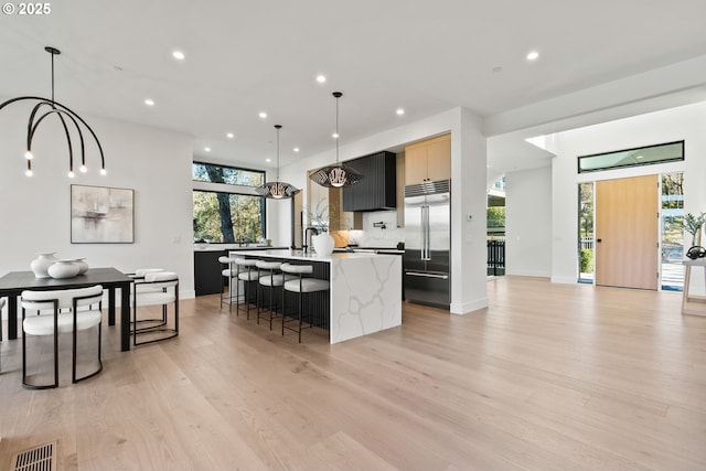 kitchen featuring hanging light fixtures, a wealth of natural light, built in fridge, and an island with sink