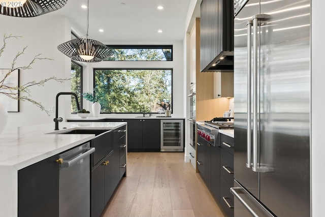 kitchen featuring wine cooler, wall chimney exhaust hood, sink, decorative light fixtures, and stainless steel appliances