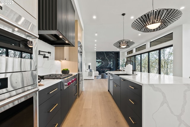 kitchen featuring sink, hanging light fixtures, appliances with stainless steel finishes, light hardwood / wood-style floors, and backsplash