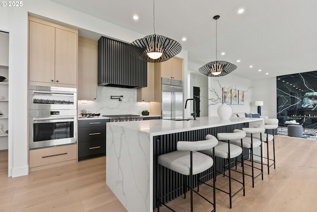 kitchen featuring stainless steel appliances, ventilation hood, hanging light fixtures, and a center island with sink