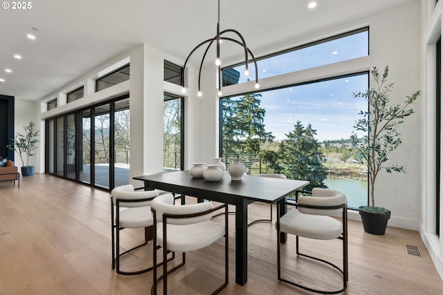 dining space with light wood-type flooring, expansive windows, and a water view