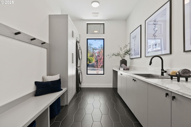 mudroom with stacked washer / dryer, sink, and dark tile patterned floors