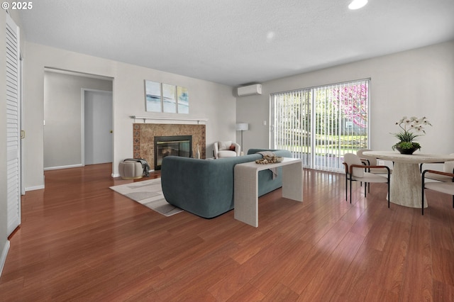 8540 SW Curry Dr Unit D, Wilsonville, OR 97070 - living room featuring a textured ceiling, baseboards, wood finished floors, a tiled fireplace, and a wall mounted air conditioner