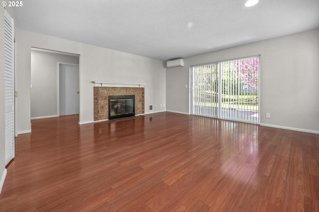 8540 SW Curry Dr Unit D, Wilsonville, OR 97070 - unfurnished living room with wood finished floors, a tile fireplace, a wall mounted air conditioner, baseboards, and a textured ceiling