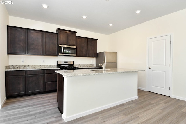 kitchen with appliances with stainless steel finishes, light wood-type flooring, dark brown cabinets, sink, and an island with sink