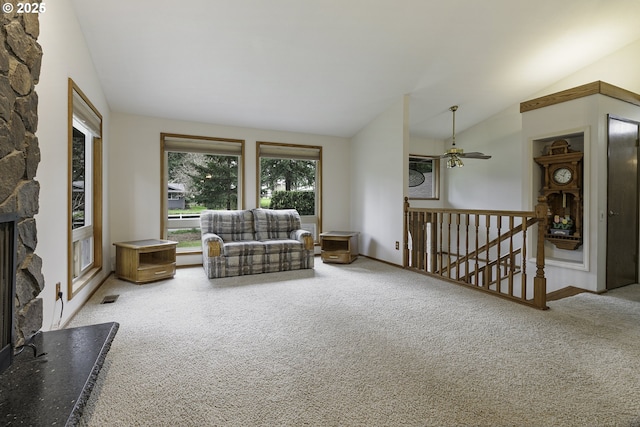 carpeted living room with visible vents, a stone fireplace, ceiling fan, and lofted ceiling