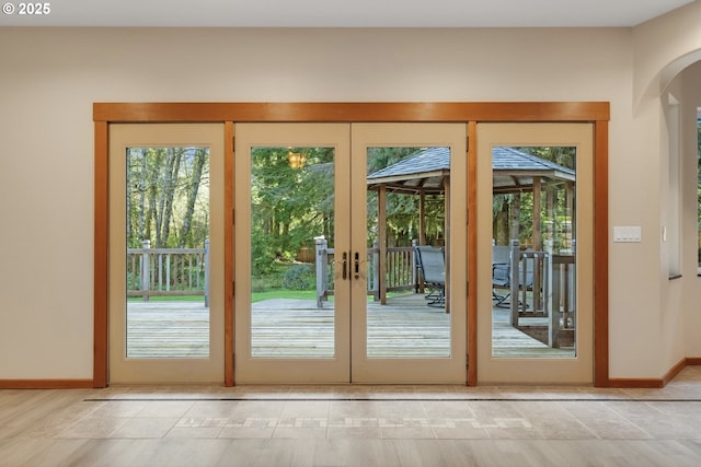 doorway with arched walkways, french doors, light tile patterned floors, and baseboards