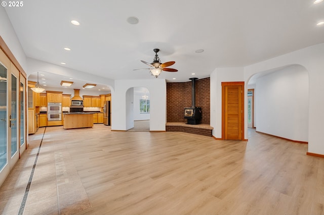 unfurnished living room with recessed lighting, arched walkways, light wood-type flooring, and a wood stove