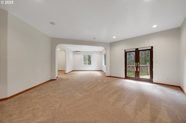empty room featuring baseboards, arched walkways, and light carpet