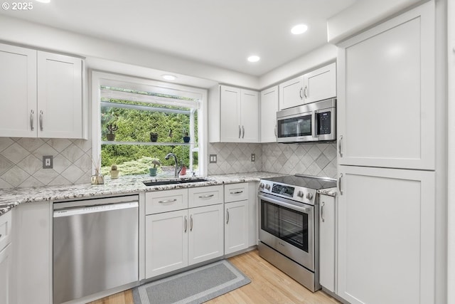16485 SW Viking Ct, Beaverton, OR 97007 - kitchen with stainless steel appliances, a sink, light wood finished floors, decorative backsplash, and light stone counters