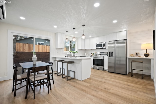 kitchen with a kitchen breakfast bar, white cabinets, light wood-type flooring, pendant lighting, and stainless steel appliances