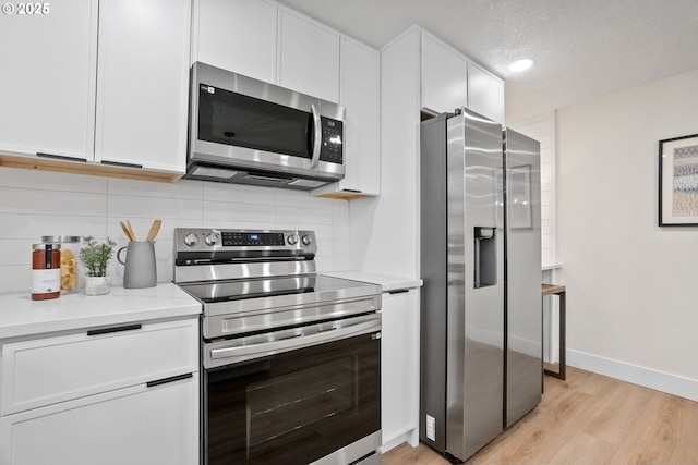 kitchen featuring a textured ceiling, light wood-type flooring, white cabinetry, and appliances with stainless steel finishes