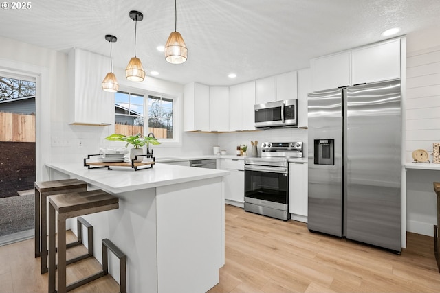 kitchen featuring appliances with stainless steel finishes, white cabinetry, a kitchen breakfast bar, kitchen peninsula, and pendant lighting