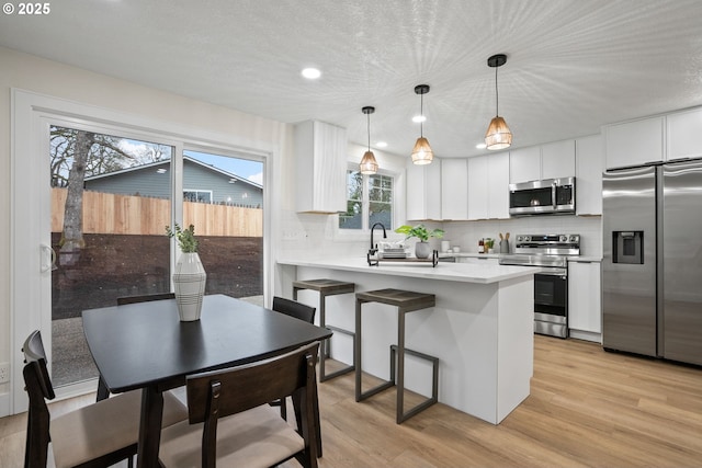 kitchen with white cabinets, kitchen peninsula, appliances with stainless steel finishes, and pendant lighting