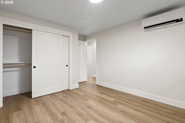 unfurnished bedroom with a wall mounted air conditioner, a closet, and light hardwood / wood-style flooring