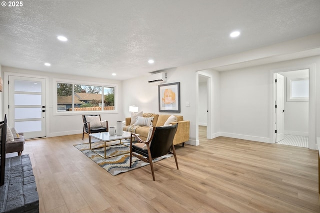 living room with an AC wall unit, a textured ceiling, and light wood-type flooring