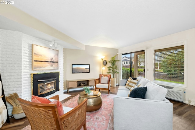 living room featuring a wall mounted air conditioner, a fireplace, and wood finished floors