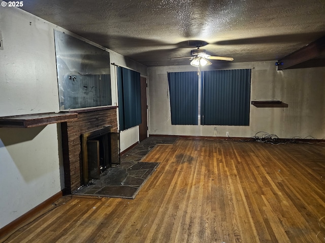 unfurnished living room featuring baseboards, a fireplace with raised hearth, ceiling fan, wood-type flooring, and a textured ceiling