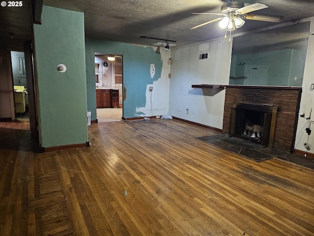 unfurnished living room with a ceiling fan, baseboards, a fireplace with raised hearth, wood-type flooring, and a textured ceiling