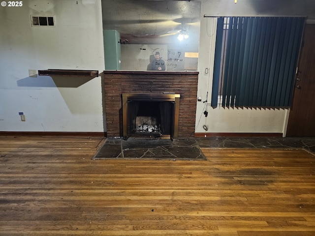 living area featuring visible vents, baseboards, a fireplace with flush hearth, and wood finished floors