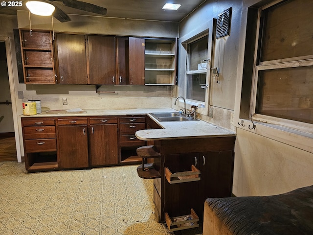 kitchen featuring open shelves, light countertops, dark brown cabinetry, and a sink