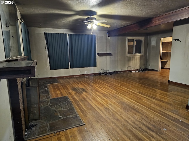 unfurnished living room featuring baseboards, wood-type flooring, a textured ceiling, and ceiling fan