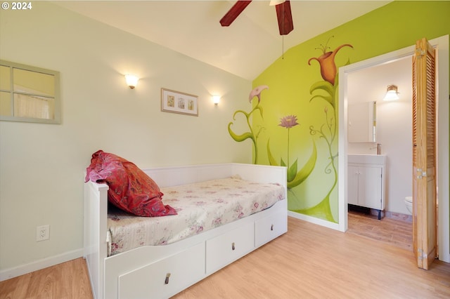 bedroom featuring wood finished floors, baseboards, ensuite bath, and lofted ceiling