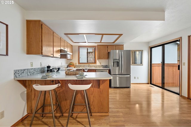 kitchen featuring a peninsula, light wood-type flooring, light countertops, under cabinet range hood, and stainless steel fridge with ice dispenser