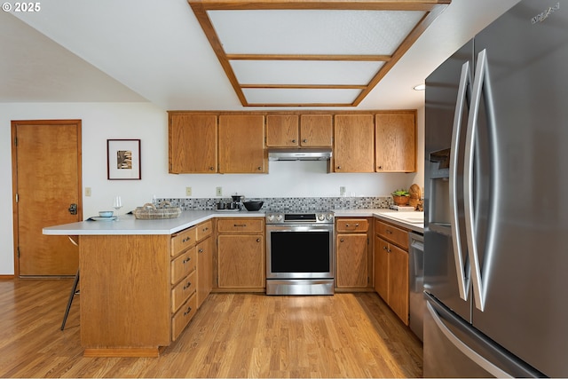 kitchen featuring light countertops, a peninsula, under cabinet range hood, light wood-style floors, and stainless steel appliances