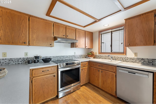 kitchen with decorative backsplash, appliances with stainless steel finishes, a sink, light wood finished floors, and under cabinet range hood