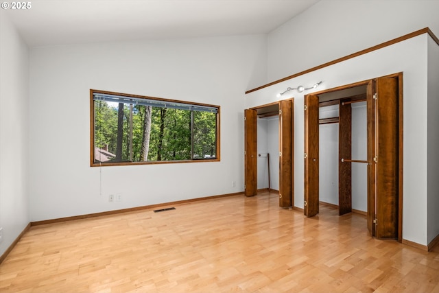 unfurnished bedroom with light wood finished floors, high vaulted ceiling, two closets, baseboards, and visible vents