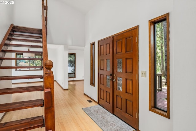 entrance foyer featuring visible vents, light wood-style floors, a towering ceiling, and stairway