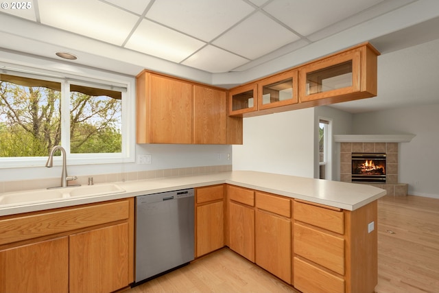 kitchen featuring a peninsula, light wood finished floors, a sink, stainless steel dishwasher, and light countertops