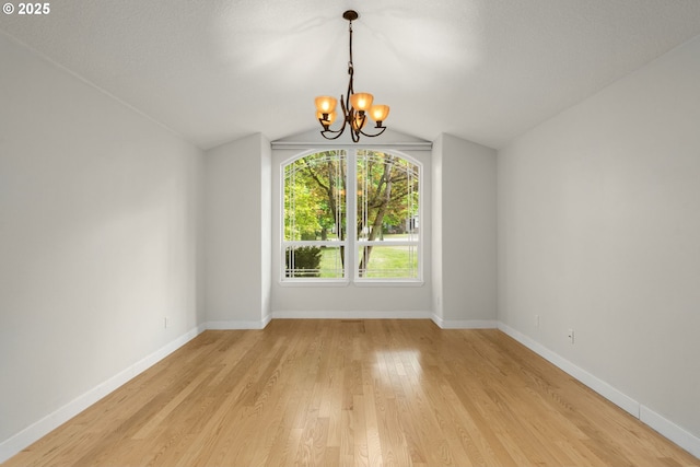 unfurnished dining area with an inviting chandelier, light wood-type flooring, baseboards, and lofted ceiling