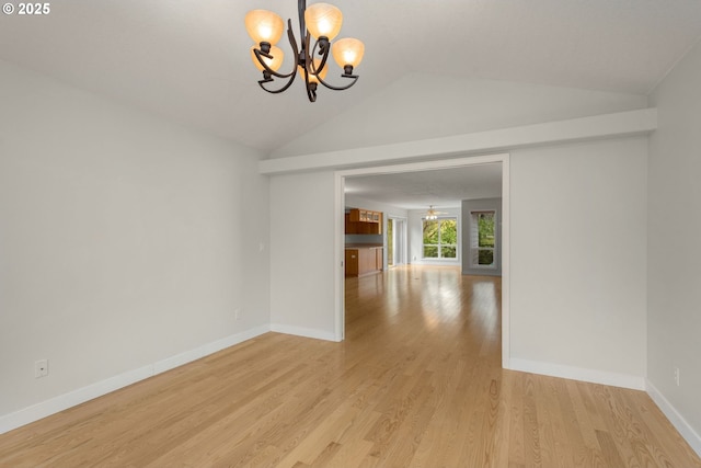 spare room featuring light wood finished floors, an inviting chandelier, baseboards, and lofted ceiling