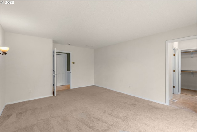 interior space with baseboards, light carpet, and a walk in closet