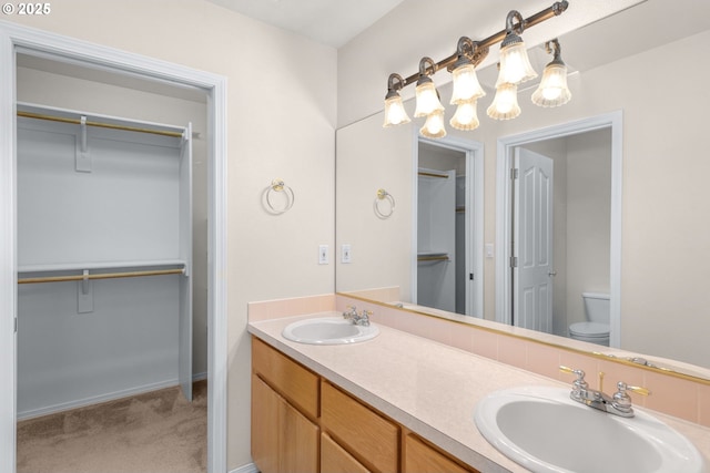 bathroom featuring a sink, double vanity, toilet, and a walk in closet